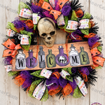 DIY Halloween wreath with purple, orange, and lime-green mesh, spooky skull accent, skull bead necklace, and Halloween WELCOME sign.
